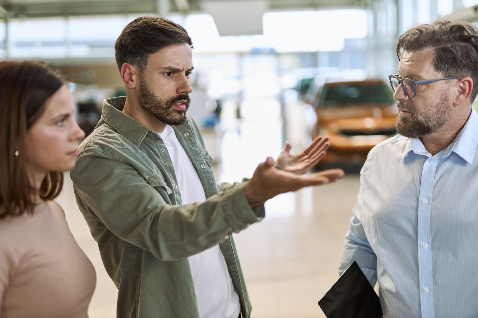 Hombre enojado y su esposa discutiendo con un vendedor de automóviles en un concesionario de automóviles.